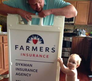 Derek and son, Kaiden, posing with Farmers Insurance signage.