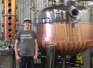 Heritage Distilling Company's 26-year-old Dain Grimmer poses next to Nonna, the distillery's impressive Italian-made copper still. Photo credit: Margo Greenman.
