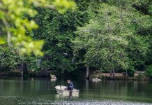 a man fishes in a small boat on Lake Sylvia, trees cover the bank on the other side